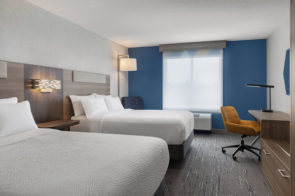 A hotel room with two beds, a desk, a chair, a lamp, and a window.