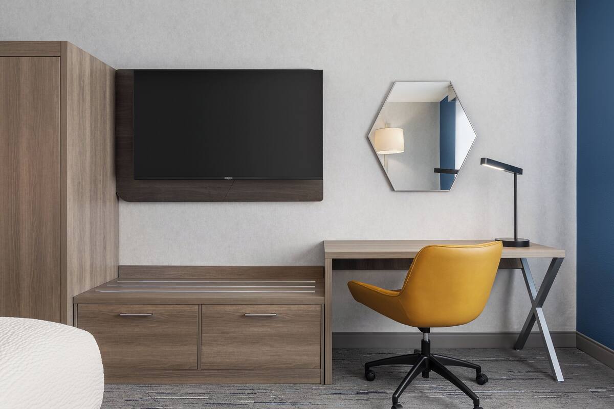 Una habitación de hotel moderna con una televisión de pantalla plana grande, un escritorio con silla, una mesita de noche y un armario.