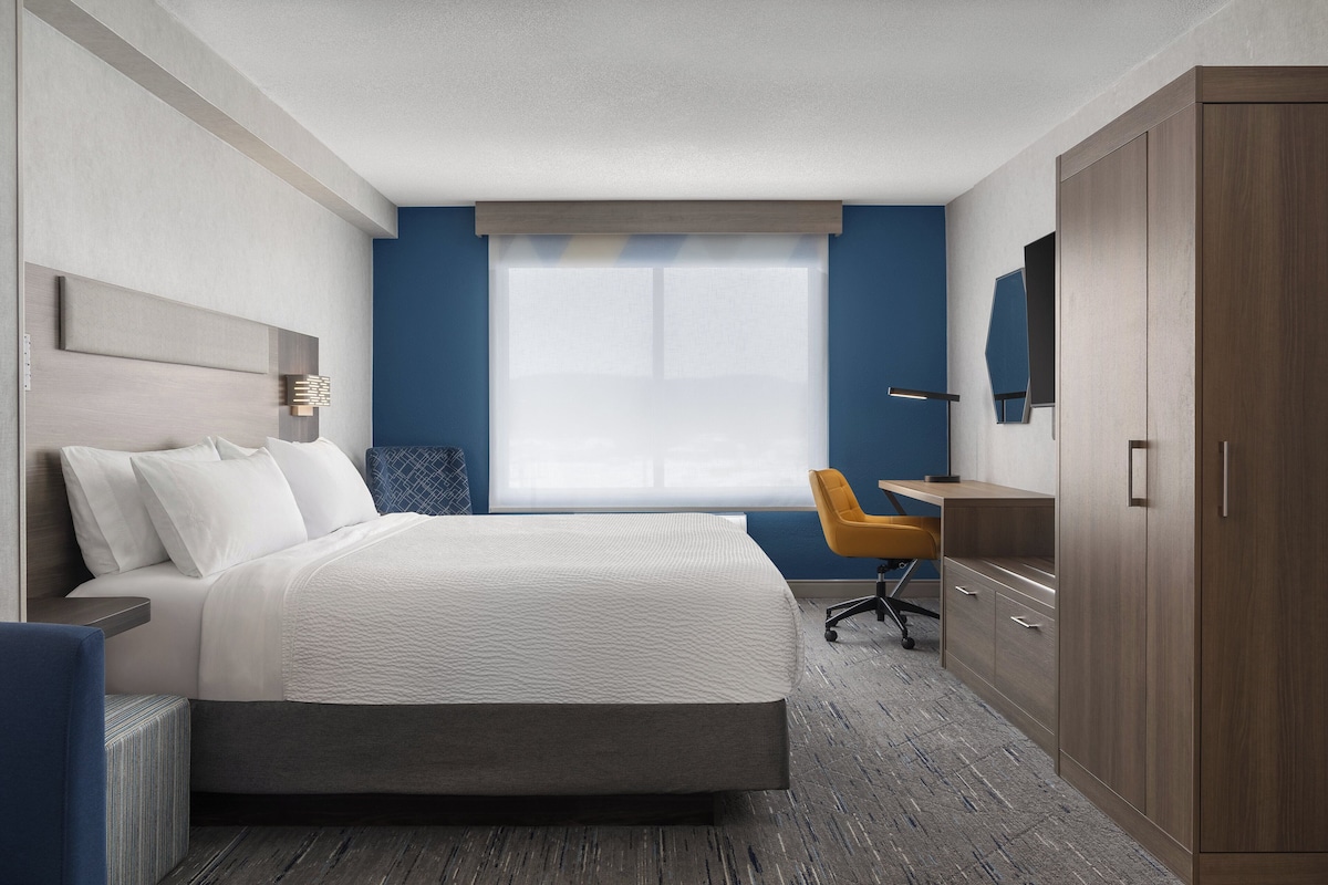 A hotel room with a bed, a desk, a chair, and a wardrobe.