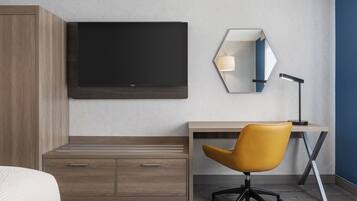 Una habitación de hotel moderna con una televisión de pantalla plana grande, un escritorio con silla, una mesita de noche y un armario.
