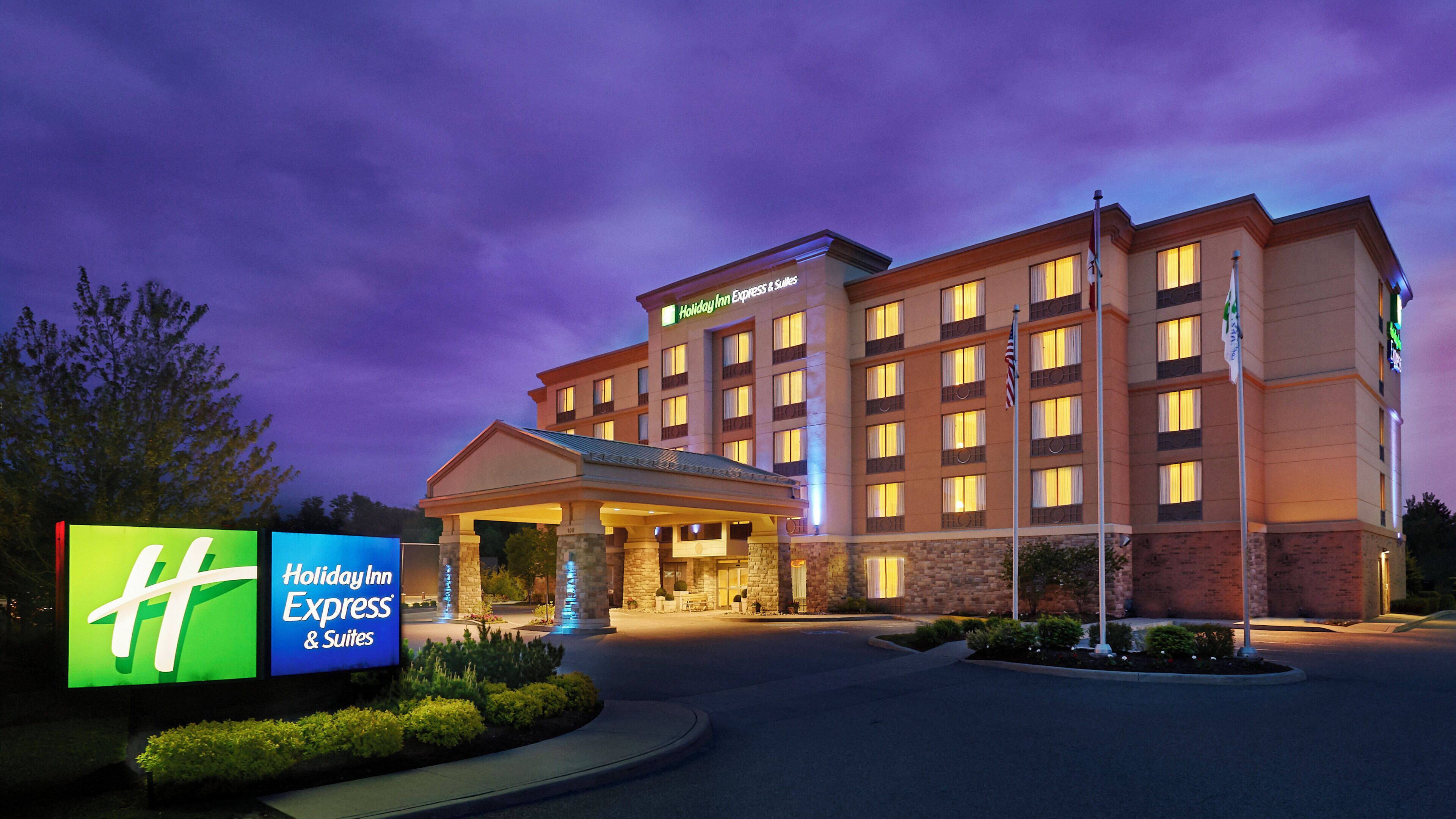 A Holiday Inn Express & Suites hotel with a well-lit entrance, a landscaped front yard, and a clear sky.