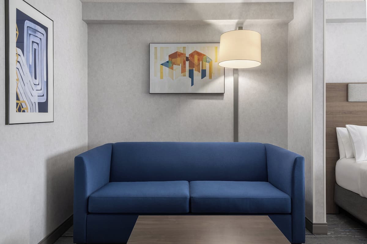 Una habitación de hotel moderna con un sofá azul, una lámpara y arte abstracto en las paredes.