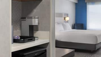 Ein Hotelzimmer mit einem Bett, einer Kaffeemaschine, einem Mülleimer und einem Regal mit einer Dose und einer Schachtel.