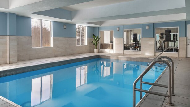An indoor swimming pool with clear blue water, a metal ladder, and a view of the outside through large windows.