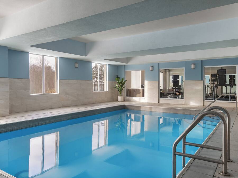 Una piscina interior amb aigua blava cristal·lina, una escala metàl·lica i vistes cap a l'exterior a través de grans finestres.