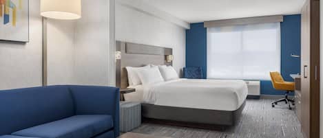 A hotel room with a bed, a blue sofa, a desk, and a window with a view.