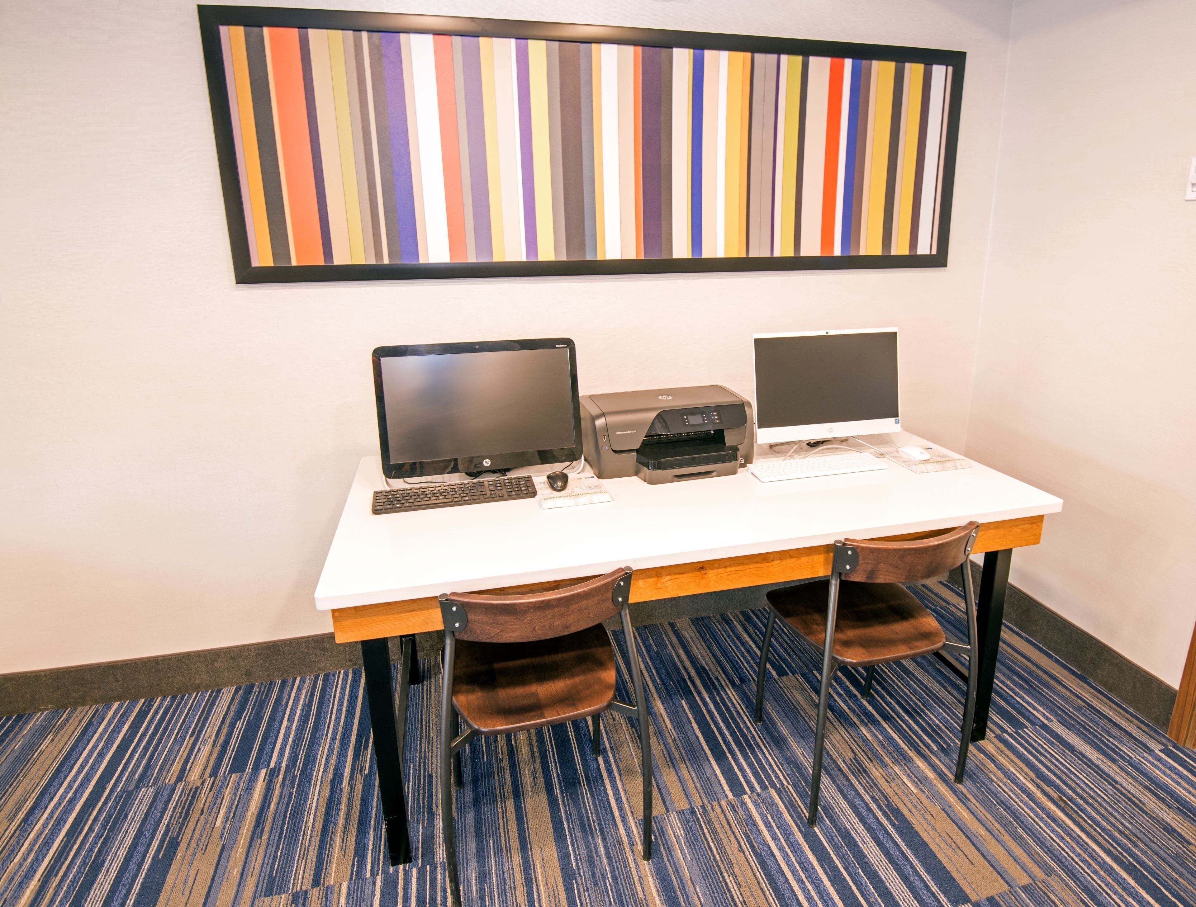 A workspace with two laptops, a printer, and a keyboard on a white table.