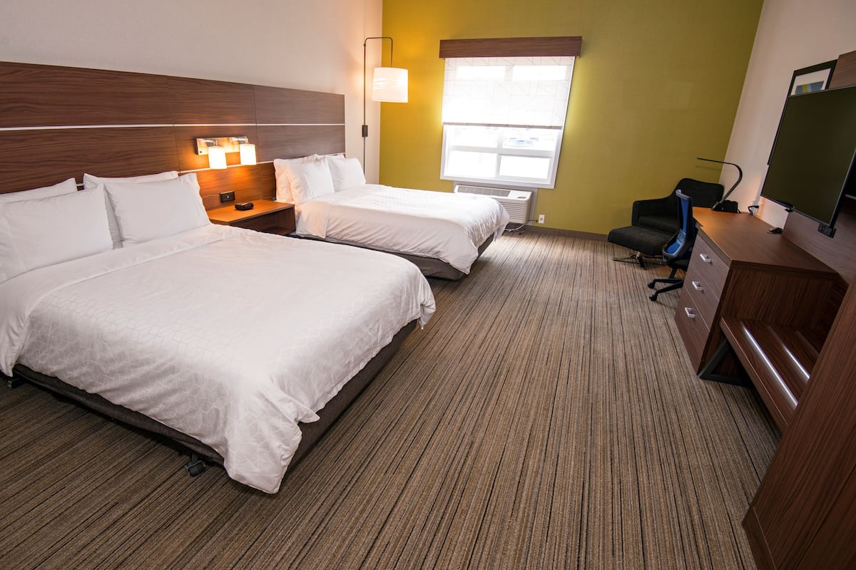 A hotel room with two beds, a desk, a chair, a TV, and a window with blinds.