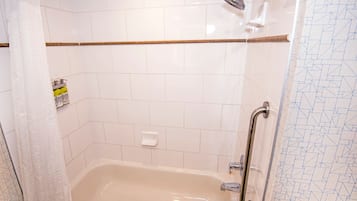 A bathroom with a bathtub, a showerhead, and a handrail.