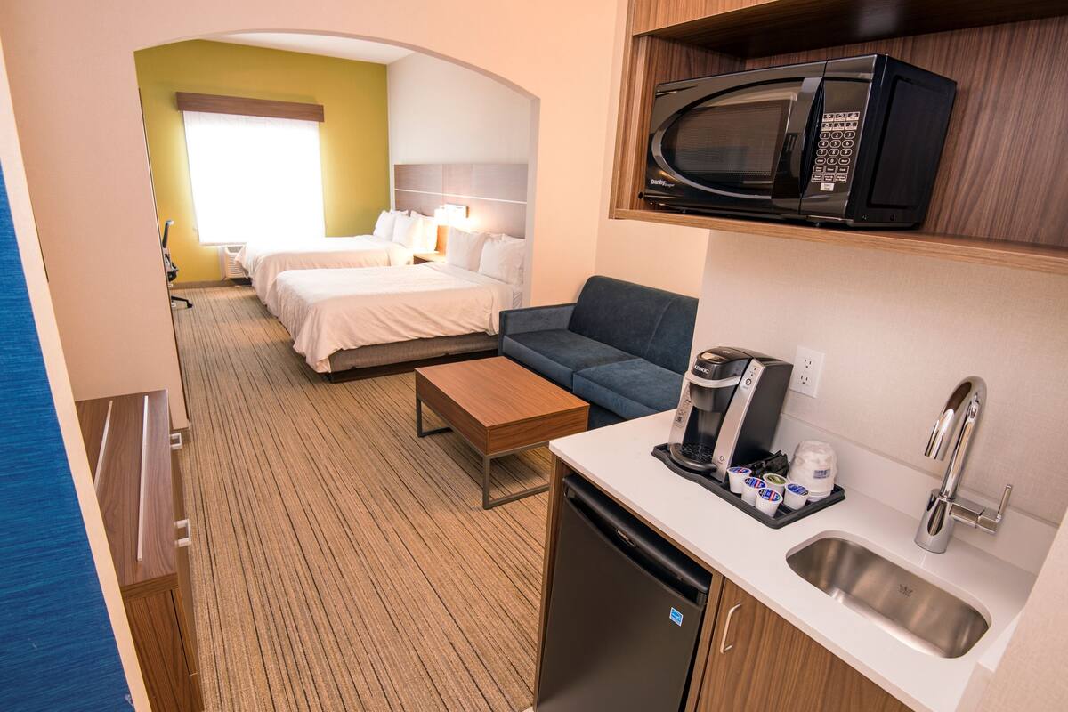 A compact hotel room with a kitchenette, a bed, a sofa, and a small dining table.