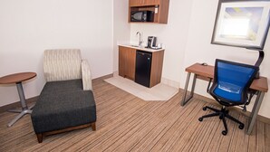 Une chambre d’hôtel de taille réduite, équipée d’une kitchenette, d’un lit simple, d’un bureau et d’une chaise.