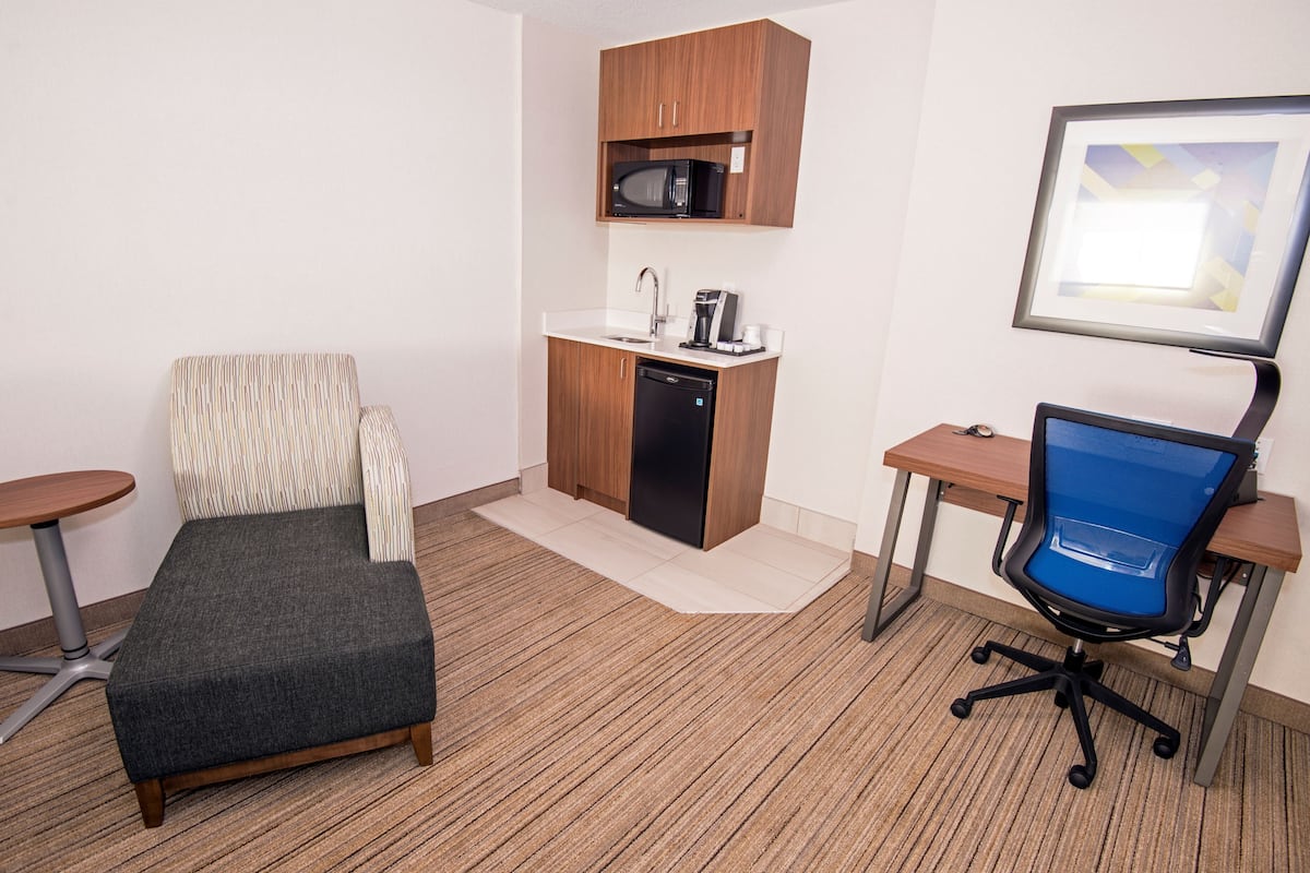 A compact hotel room with a kitchenette, a single bed, a desk, and a chair.