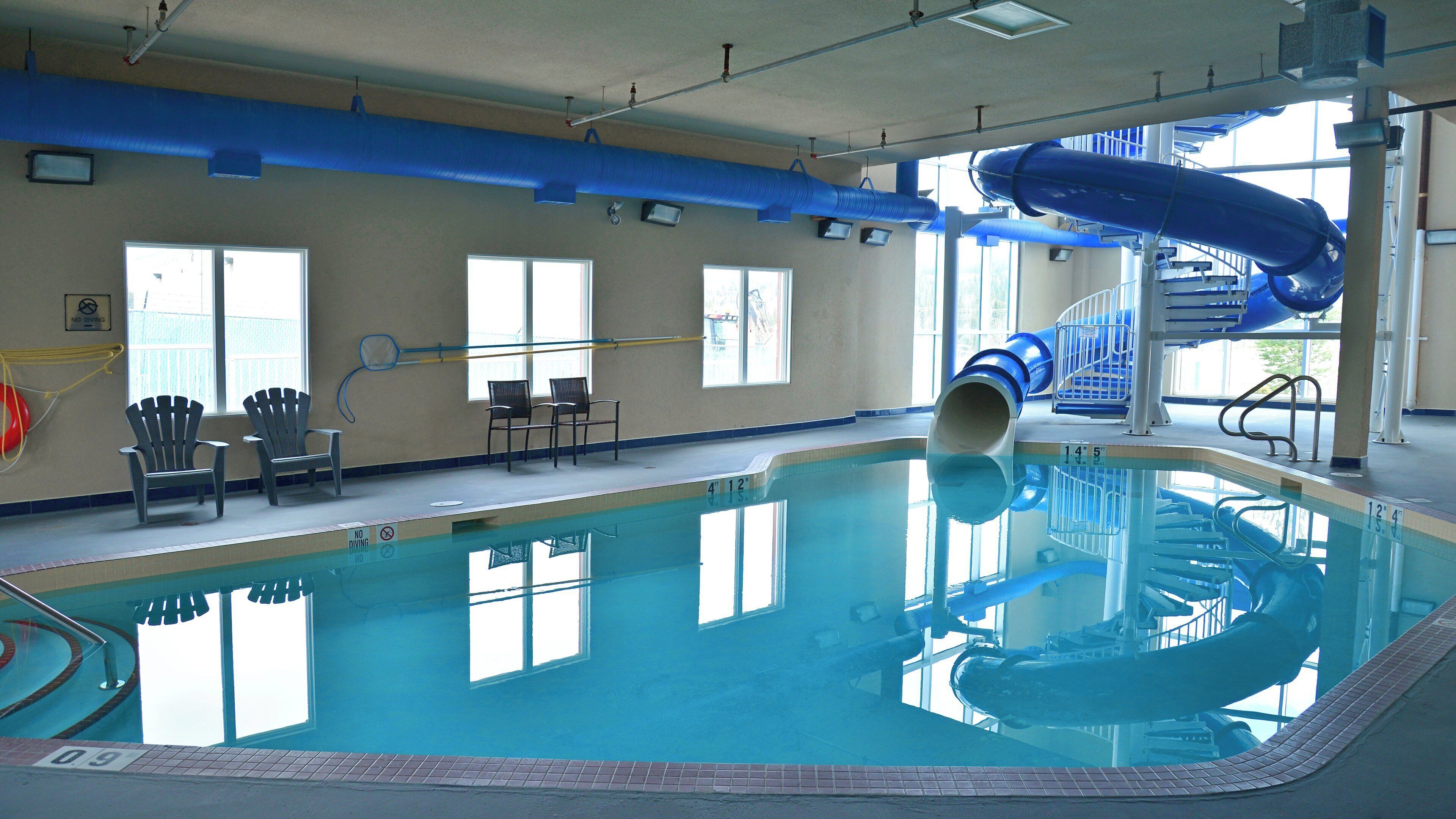 Una piscina interior con tobogán, sillas y un cartel de prohibido bucear.