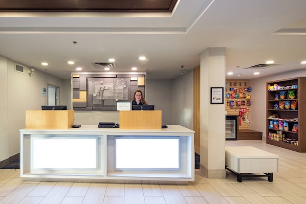 A hotel reception area with a modern design, a reception desk, a small refrigerator, and a snack shelf. - Holiday Inn Express Hotel & Suites Hinton by IHG (Hinton)