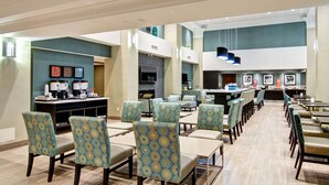 Un grand espace dédié à la salle à manger, avec plusieurs tables et chaises, un coin café et un téléviseur fixé au mur.
