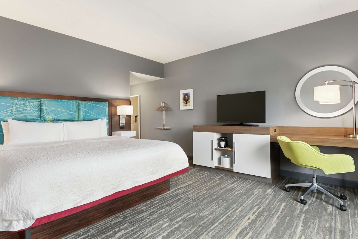 Ein Hotelzimmer mit einem Bett, einem Schreibtisch mit Stuhl, einem Fernseher, einer Lampe und einem Bild an der Wand.