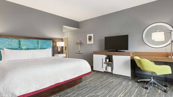Habitación de hotel con cama, escritorio con silla, televisor, lámpara y un cuadro en la pared.