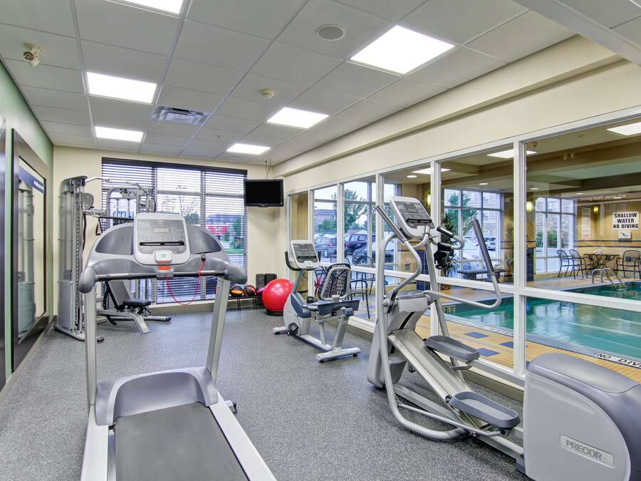 A gym with treadmills, elliptical machines, and a stationary bike, with a pool visible through the windows.