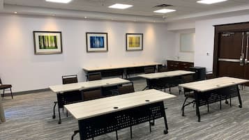 Un salón de conferencias con varias mesas y sillas, paredes blancas e iluminación en el techo.