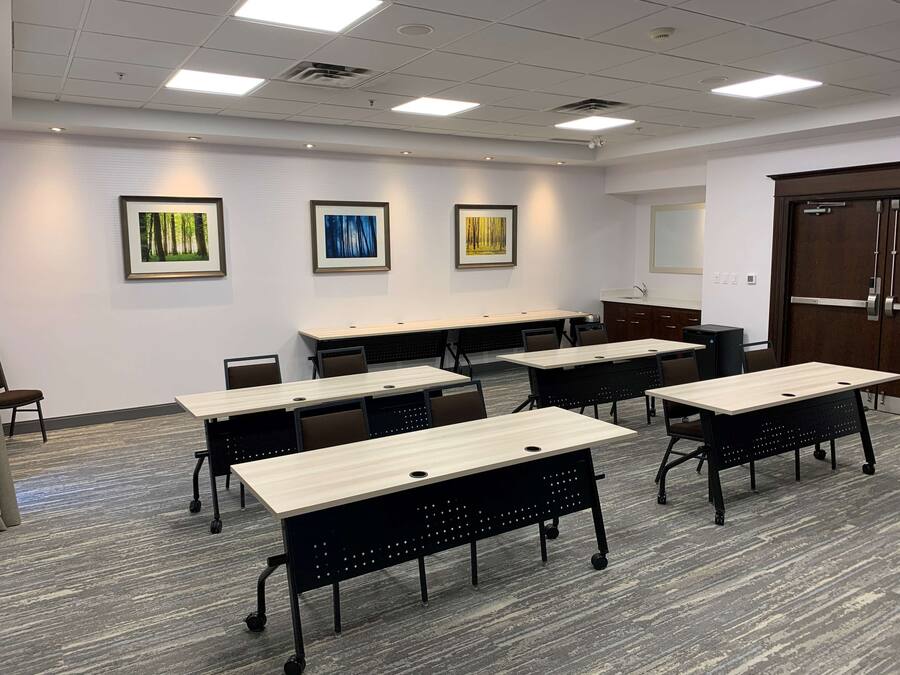 Uma sala de conferências com várias mesas e cadeiras, paredes brancas e iluminação no teto.