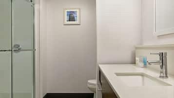 Un baño moderno con cabina de ducha de vidrio, inodoro blanco y lavamanos con grifo cromado.
