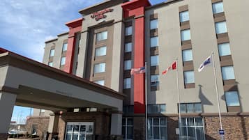 Um hotel Hampton Inn com entrada desobstruída, bandeiras americana e canadense, e placa de estacionamento para deficientes.