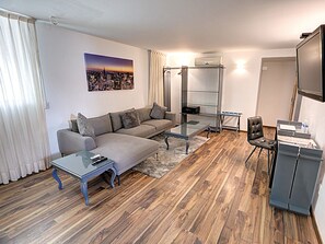 A modern living room with a grey sofa, a glass coffee table, and a wooden floor.