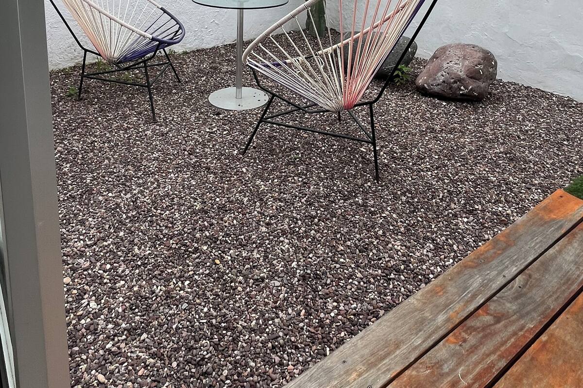 A small outdoor seating area with two metal chairs and a table, surrounded by gravel and a cactus.