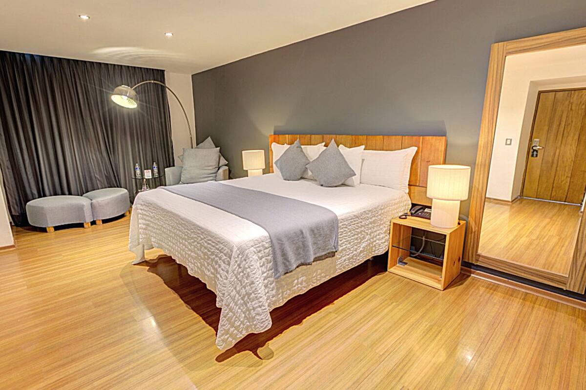 A modern bedroom with a large bed, bedside tables, a mirror, and a dark curtain backdrop.