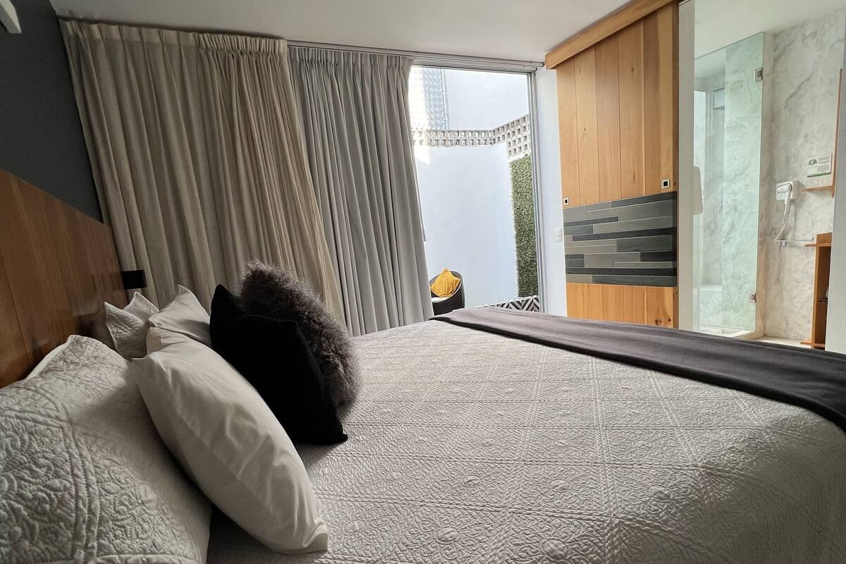 A modern hotel room with a large bed, a view of the outdoors, and a sliding glass door leading to a balcony.