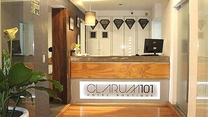 A hotel reception area with a wooden reception desk, a potted plant, and a sign reading "CLARUM101 HOTEL BOUTIQUE". - Hotel CLARUM 101 (Zapopan)