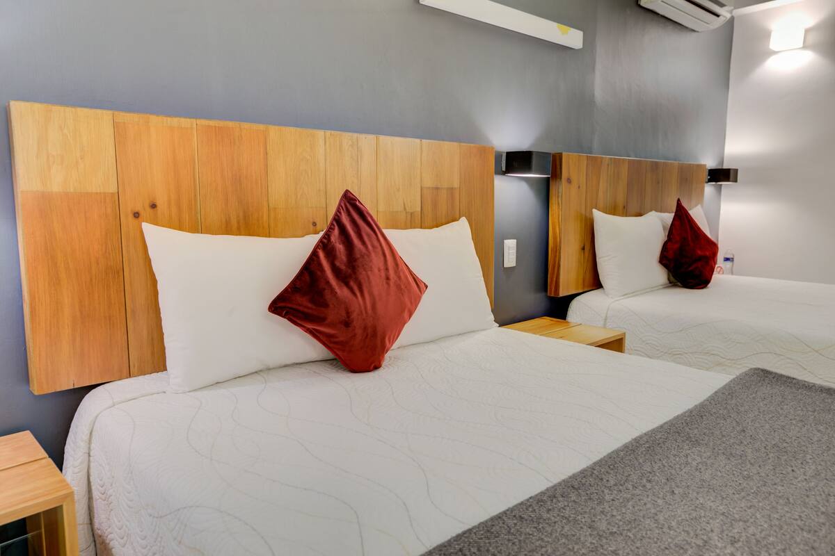 A hotel room with two beds, wooden headboards, and a grey carpet.