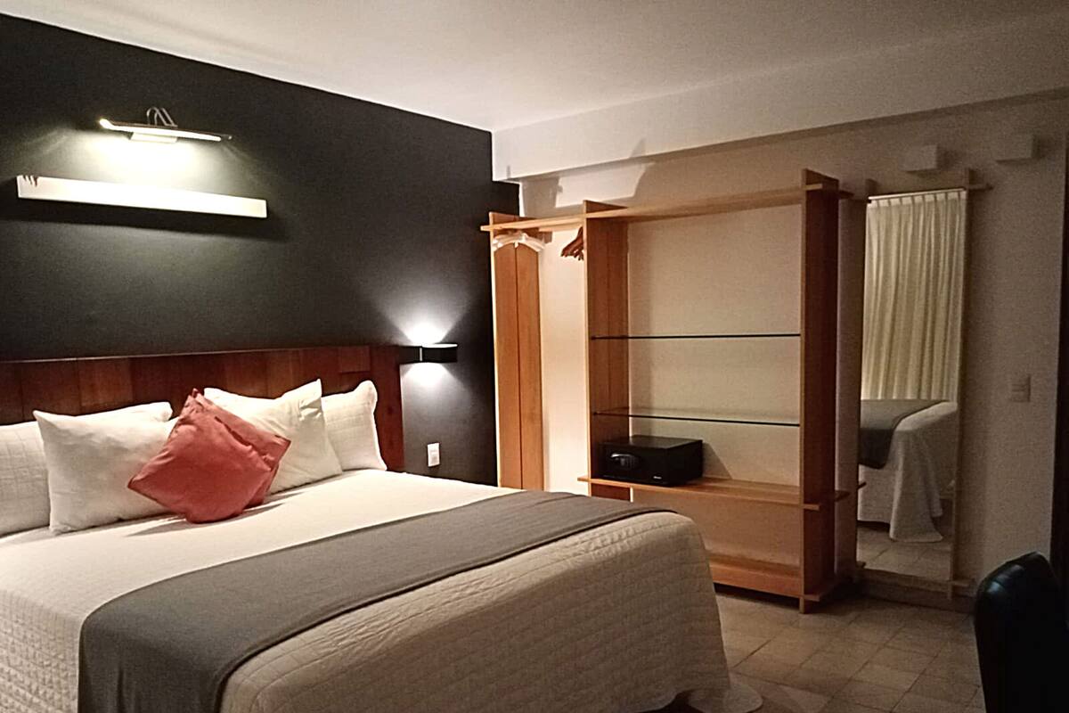 A hotel room with a bed, bedside table, and a wardrobe with a mirror.