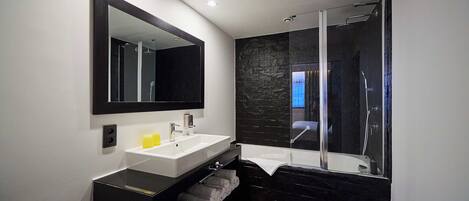A modern bathroom with a large mirror, a sink, a bathtub, and a shower area.