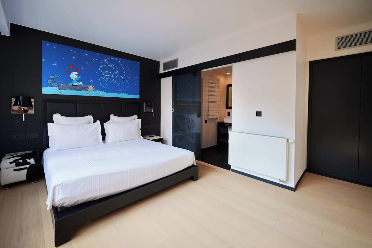 A modern bedroom with a large bed, a nightstand, a wall-mounted TV, and a sliding door leading to a bathroom.