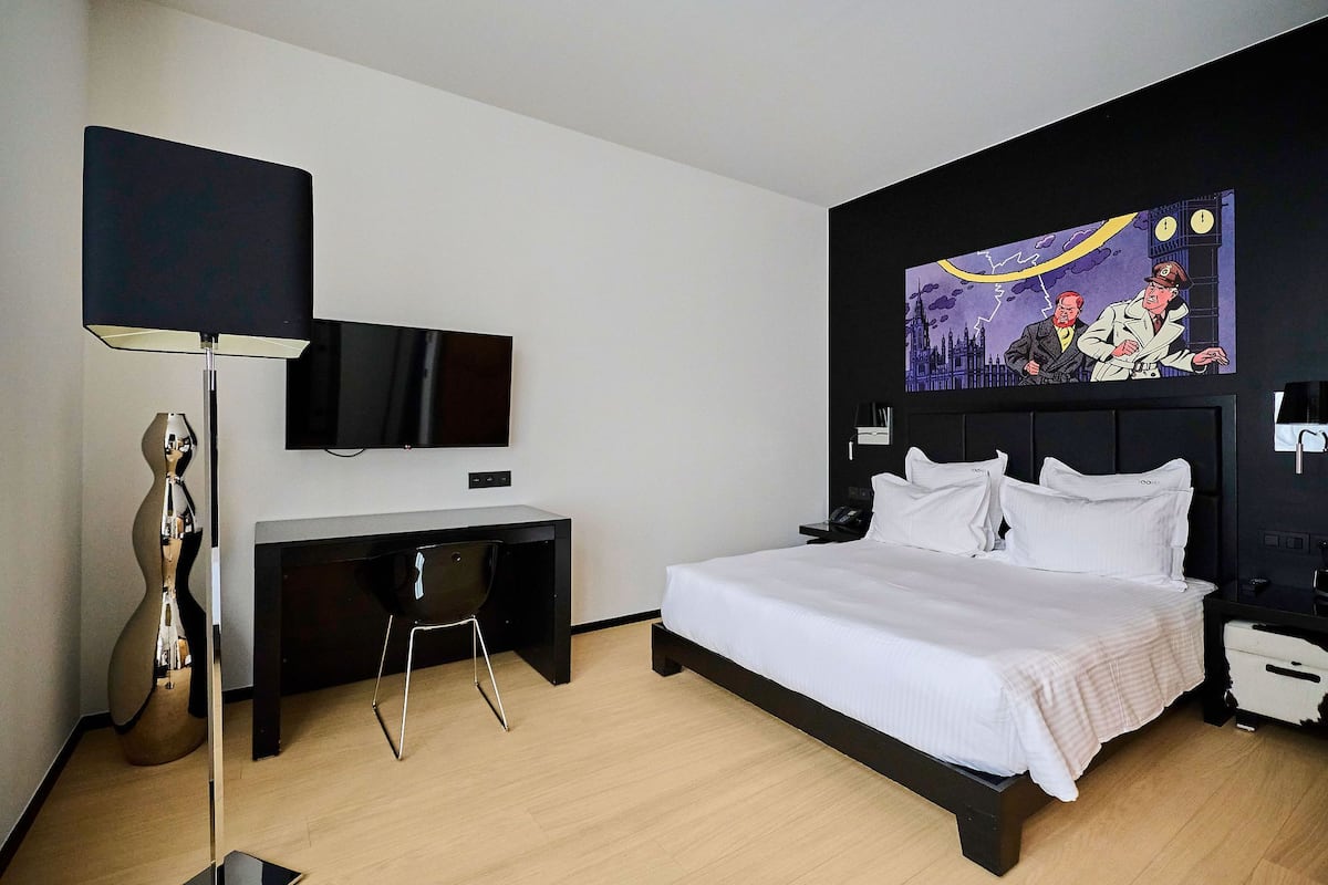 A modern hotel room with a bed, desk, chair, and a flat-screen TV.