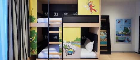 Habitación con literas, una escalera, un pequeño estante y una pared decorada con un personaje de caricatura.