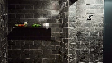 Bathroom features a dark stone wall design, a mounted shelf, and dark stone tile flooring.