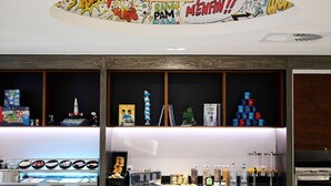 A hotel reception area with a comic book-themed ceiling, a display of books and figurines, and a counter with various food items and condiments. - YOOMA Urban Lodge (Brussels)