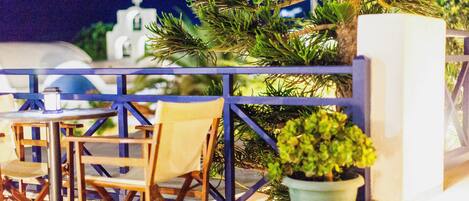Una terraza con sillas y mesas de madera, una planta en maceta y vistas a un edificio de paredes blancas y una cúpula.