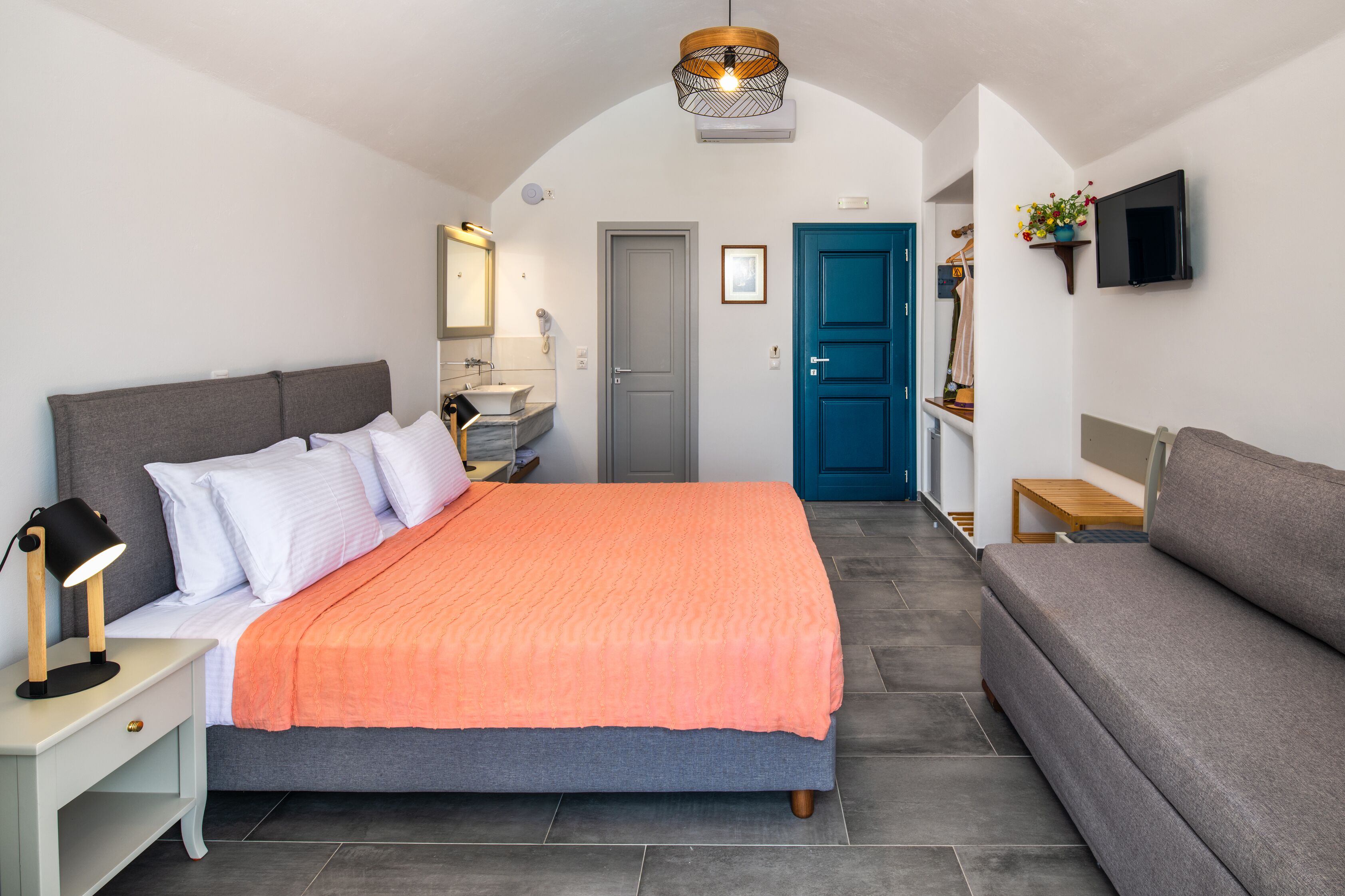 Ein Schlafzimmer mit Bett, Nachttisch, Lampe und einem an der Wand befestigten Fernseher.