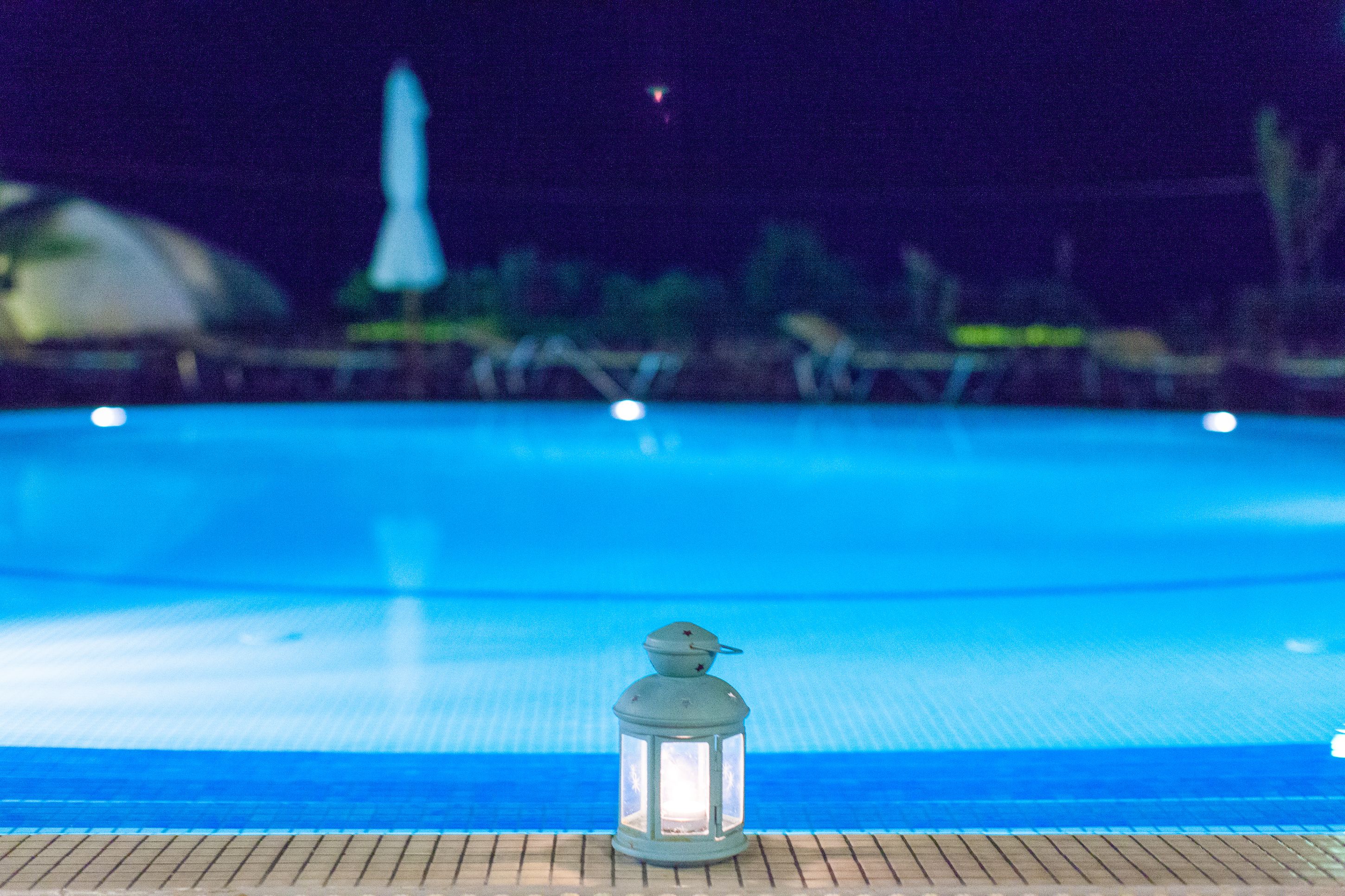 A nighttime view of a swimming pool with a lantern in the foreground.