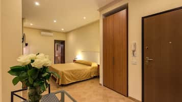 A hotel room with a bed, a wooden wardrobe, a nightstand, a lamp, and a vase with flowers.