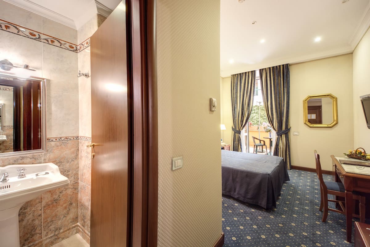A hotel room with a marble bathroom, a bed with a dark bedspread, a dining table with chairs, and a large mirror on the wall.