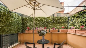Une terrasse avec une table et des chaises, entourée d’un mur recouvert de lierre et agrémentée de plantes en pot.