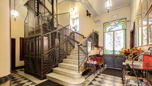 Un grand escalier orné d’une rampe en métal, doté d’un sol à carreaux et d’une fenêtre en vitrail.