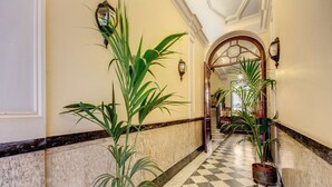 Un couloir doté d’un sol en marbre, de plantes en pot et d’un motif à carreaux.