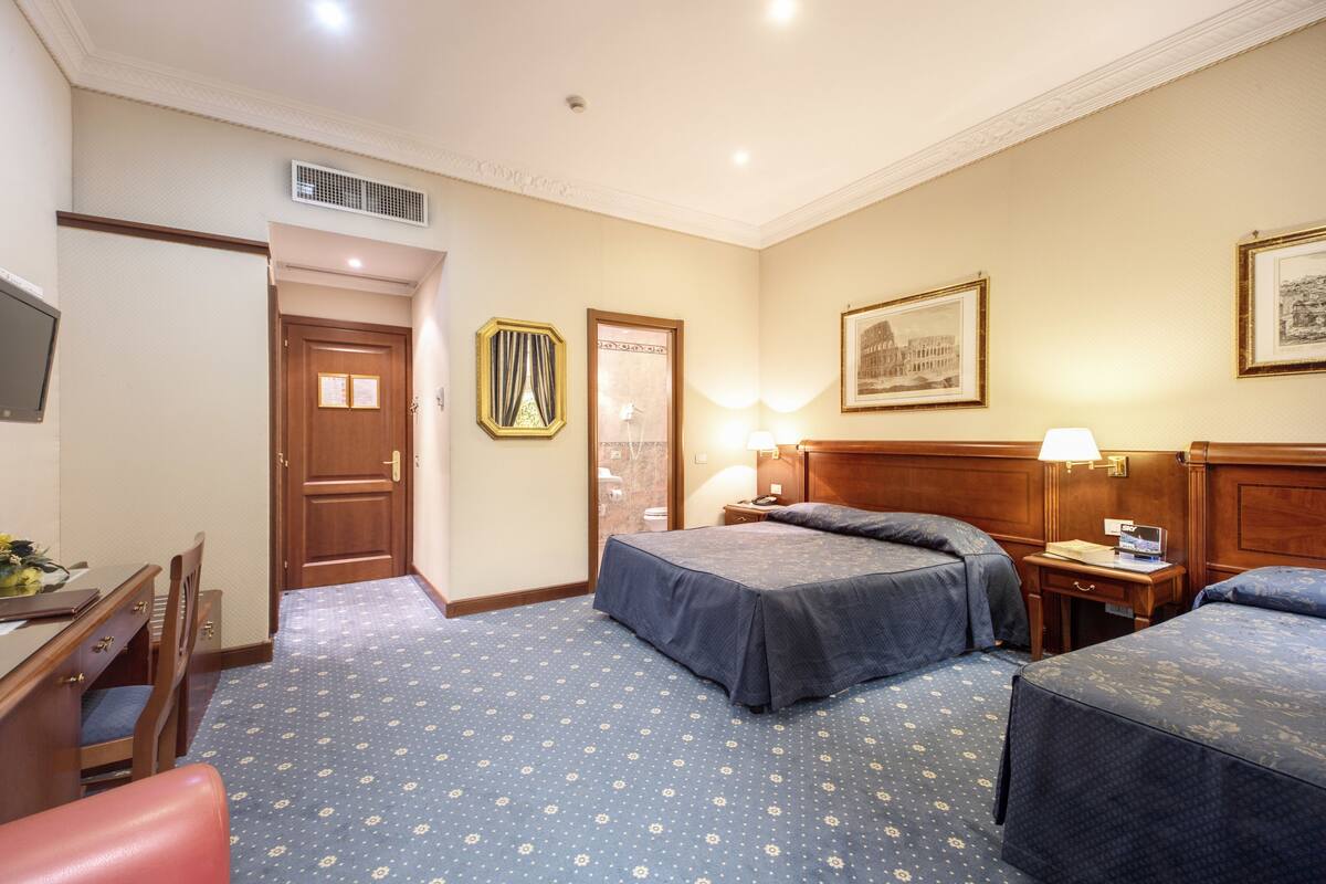 A hotel room with two beds, a desk, a chair, and a television.
