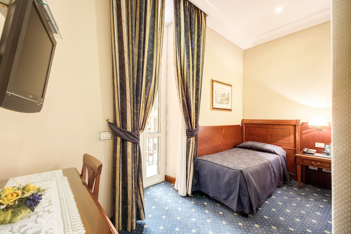 A hotel room with a bed, a desk, a chair, a television, and curtains.