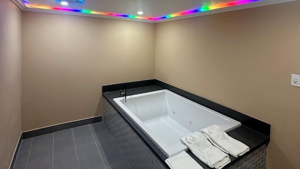 Et moderne badeværelse med et rektangulært badekar, sort flisegulv og et loft med flerfarvede LED-lys.